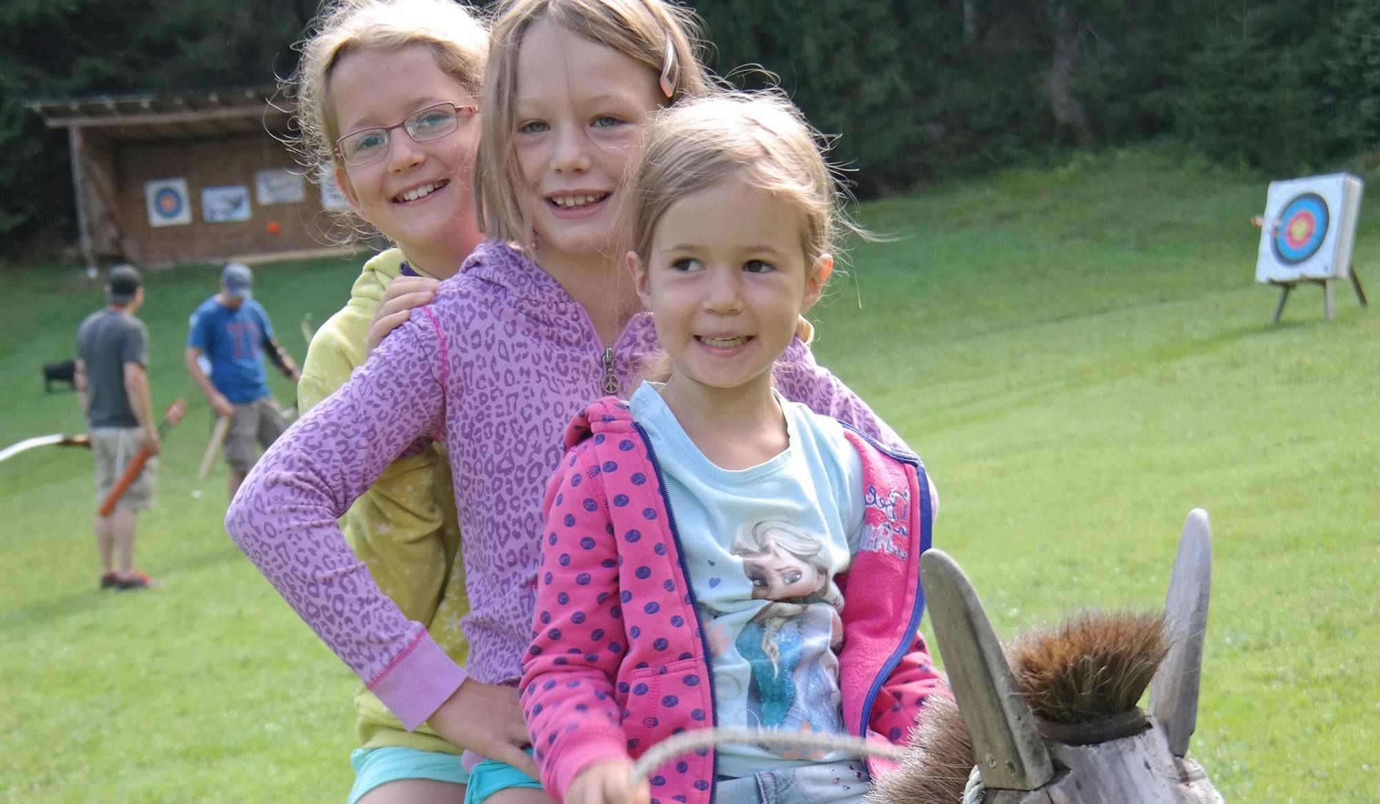 Drei Mädels auf einem Holzpferd haben Spaß beim Sommerurlaub am Heisshof