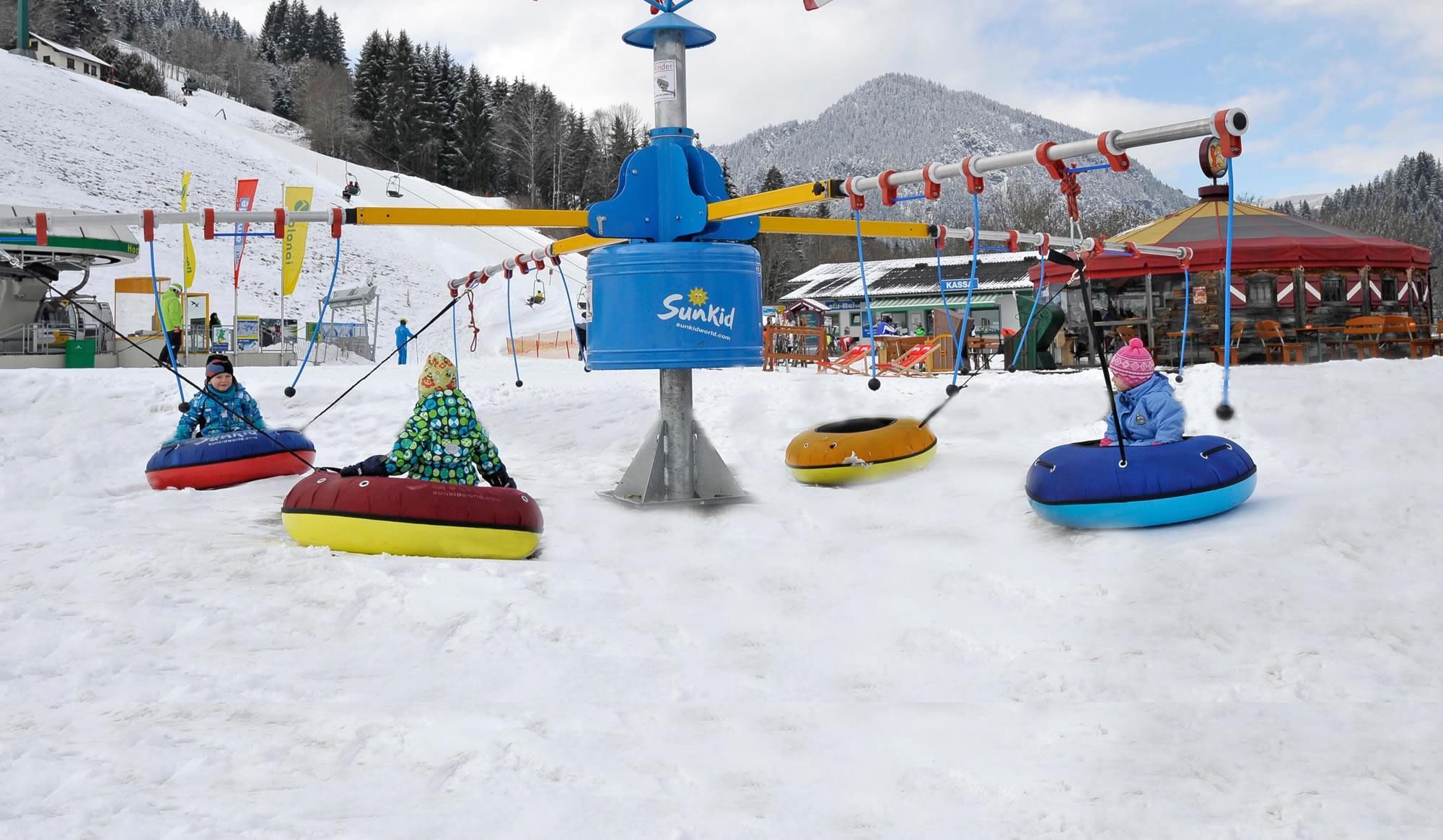 Kinder sitzen auf Snowtubes und werden vom Kinderkarussell im Kreis gezogen